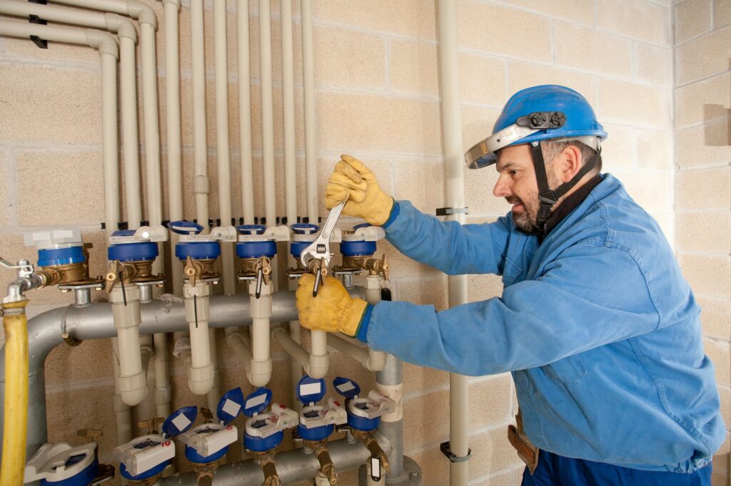 A technician works on plumbing valves in a utility room during the day